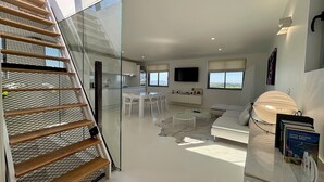A modern interior with a glass staircase, a dining area, a living room with a sofa, and a TV mounted on the wall. - White Loft - 6 personnes - toit-terrasse avec vue panoramique (Donzenac)
