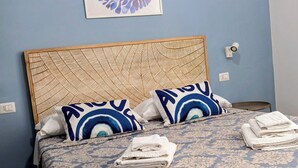 Ein ordentlich bezogenes Bett, Bettwäsche mit Muster, zwei Kissen mit blau-weißem Design und ein gerahmtes Kunstwerk an der Wand darüber.