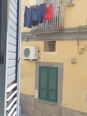 Un balcón con ropa tendida, una ventana con contraventanas y un equipo de aire acondicionado.