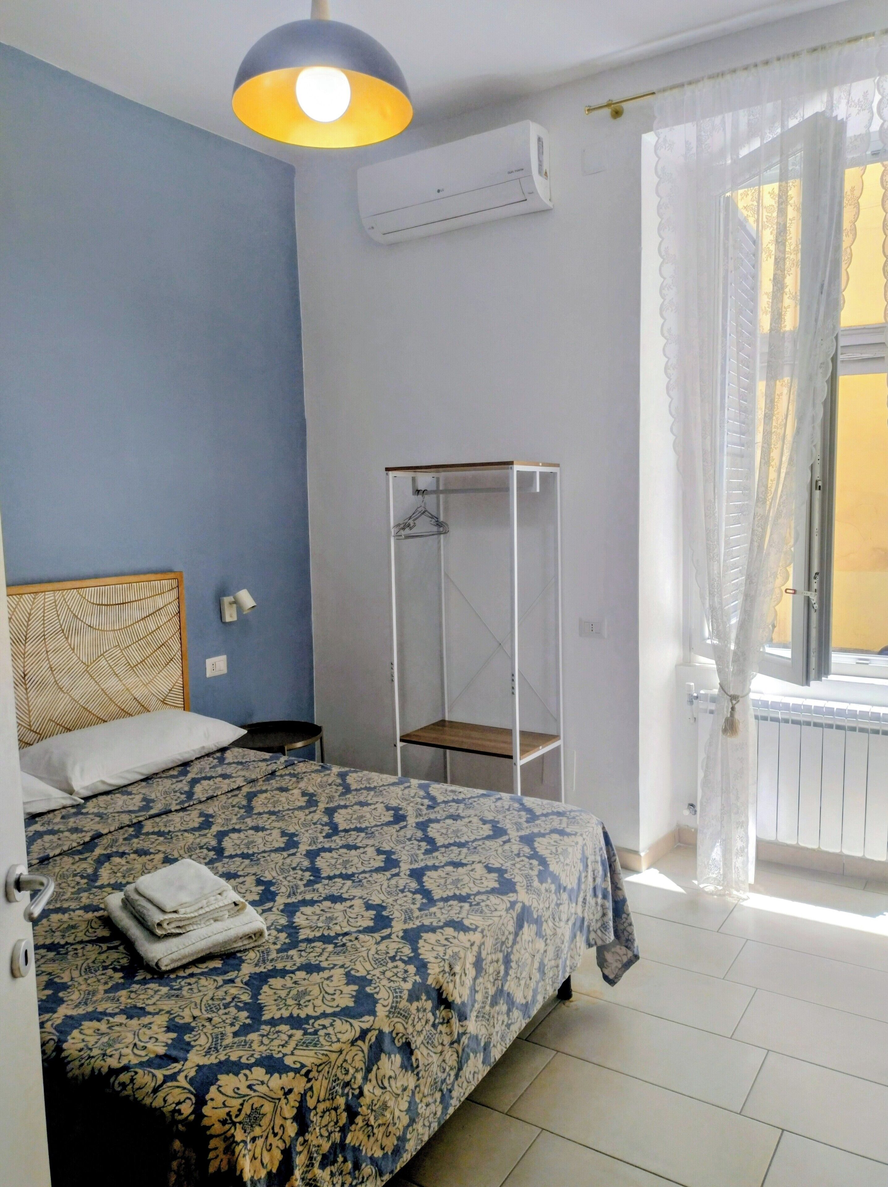 Ein Schlafzimmer mit Bett, Kleiderstange, einem Fenster mit Vorhängen und einer Klimaanlage.