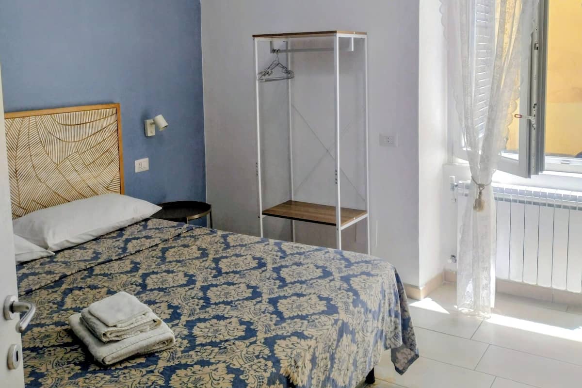 Ein Schlafzimmer mit Bett, Kleiderstange, einem Fenster mit Vorhängen und einer Klimaanlage.