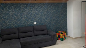 Ein Zimmer mit einem dunkelgrauen Sofa, einer Wand mit Muster und einem Rubik's Cube auf dem Boden.