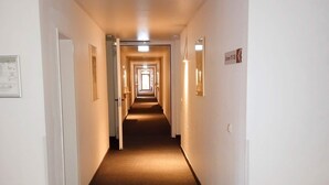Hotellin käytävä, jossa on ovia molemmilla puolilla, matolla peitetty lattia ja kyltti, jossa on merkitty huoneen numero 123.