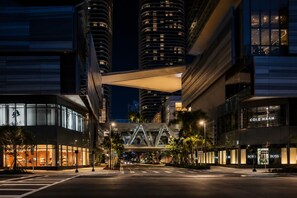 A modern urban street at night with illuminated buildings, a pedestrian bridge, and storefronts including a Cole Haan store. - Luxury Miami Stay with Skyline Balcony (Miami)