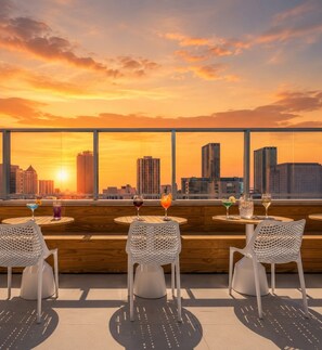 A rooftop bar with white mesh chairs and tables, offering a sunset view of a city skyline. - Luxury Miami Stay with Skyline Balcony (Miami)