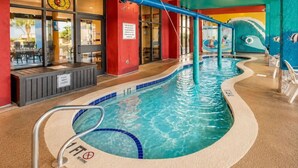 En indendørs swimmingpool med et forbudsskilt mod dykning, et sikkerhedsskilt og et poolområde med restaurant.