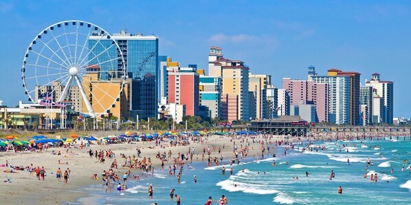 A beach with a Ferris wheel, a city skyline, and a crowded beach. - Oceanfront Suite • Balcony • Pools • Monterey Bay (Myrtle Beach)