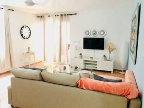 Ein Wohnzimmer mit einer Couch, einem Couchtisch, einem Fernseher und einer Wanduhr.
