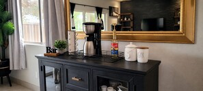 Eine Küchenarbeitsplatte mit Kaffeemaschine, Zucker- und Kaffeegläsern, einem Bartischschild und einer Pflanze.