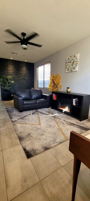 Ein Wohnzimmer mit einer schwarzen Ledersofa, einem Kamin, einem Deckenventilator und einer Steinwand.