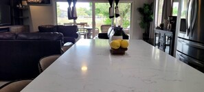 Eine moderne Küche mit Marmorarbeitsplatte, ein Essbereich mit Ledersofa und Blick ins Freie.