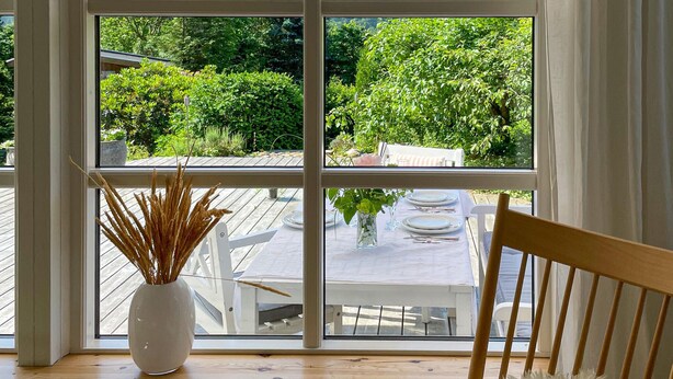 Una ventana con vista a una terraza de madera y mobiliario exterior.