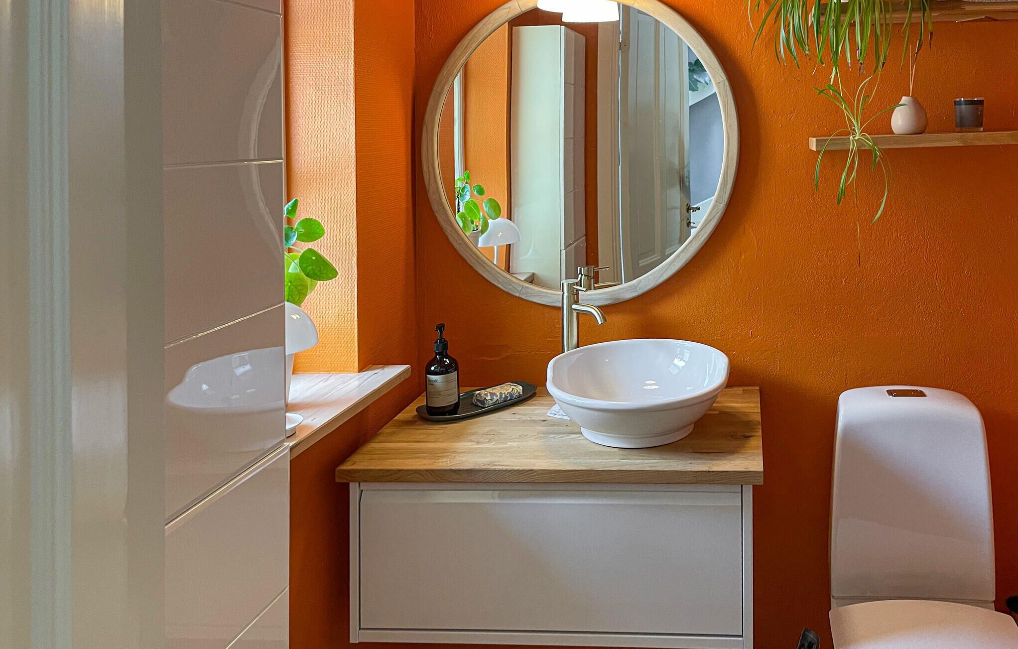 A bathroom with a round mirror, white sink, and a toilet.