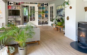 A cozy living room with a fireplace, bookshelves, and potted plants. - 3 bedroom beautiful home in Bryrup (Bryrup)