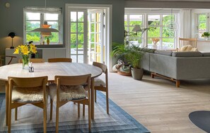 A dining area with a round table, chairs, and a vase of flowers. There is a sofa and a window with a view of greenery. - 3 bedroom beautiful home in Bryrup (Bryrup)