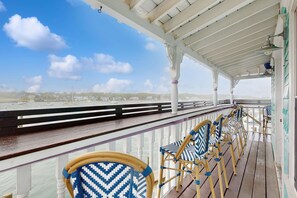 A covered outdoor area with a railing, wooden chairs, and a view of a body of water and distant buildings.