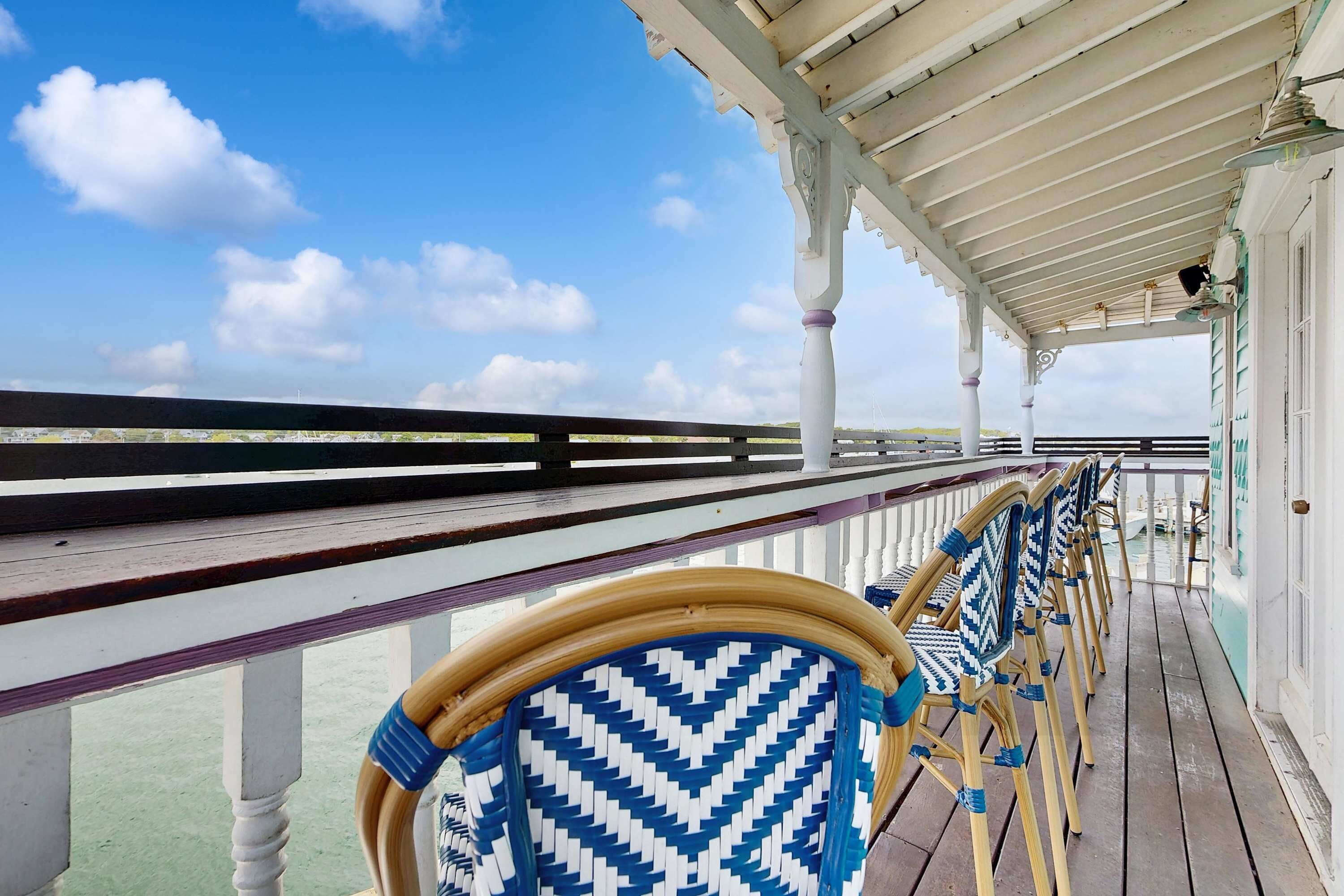 Un espace extérieur abrité, doté d’une rambarde, de chaises en bois aux motifs bleus et blancs, et offrant une vue sur la mer.