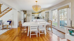 A spacious kitchen with white cabinetry, a dining area with white chairs, and a wooden staircase. - Walk to Grays Beach, Near Shops & Boardwalk (Yarmouth)