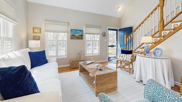 A spacious living room with a white sofa, blue cushions, a woven coffee table, and a staircase with wooden railings. - Walk to Grays Beach, Near Shops & Boardwalk (Yarmouth)