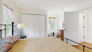 A bedroom with a bed, a nightstand, a dresser, a lamp, and a window with curtains.