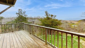 A wooden deck with a railing, overlooking a landscape with trees and a distant view.