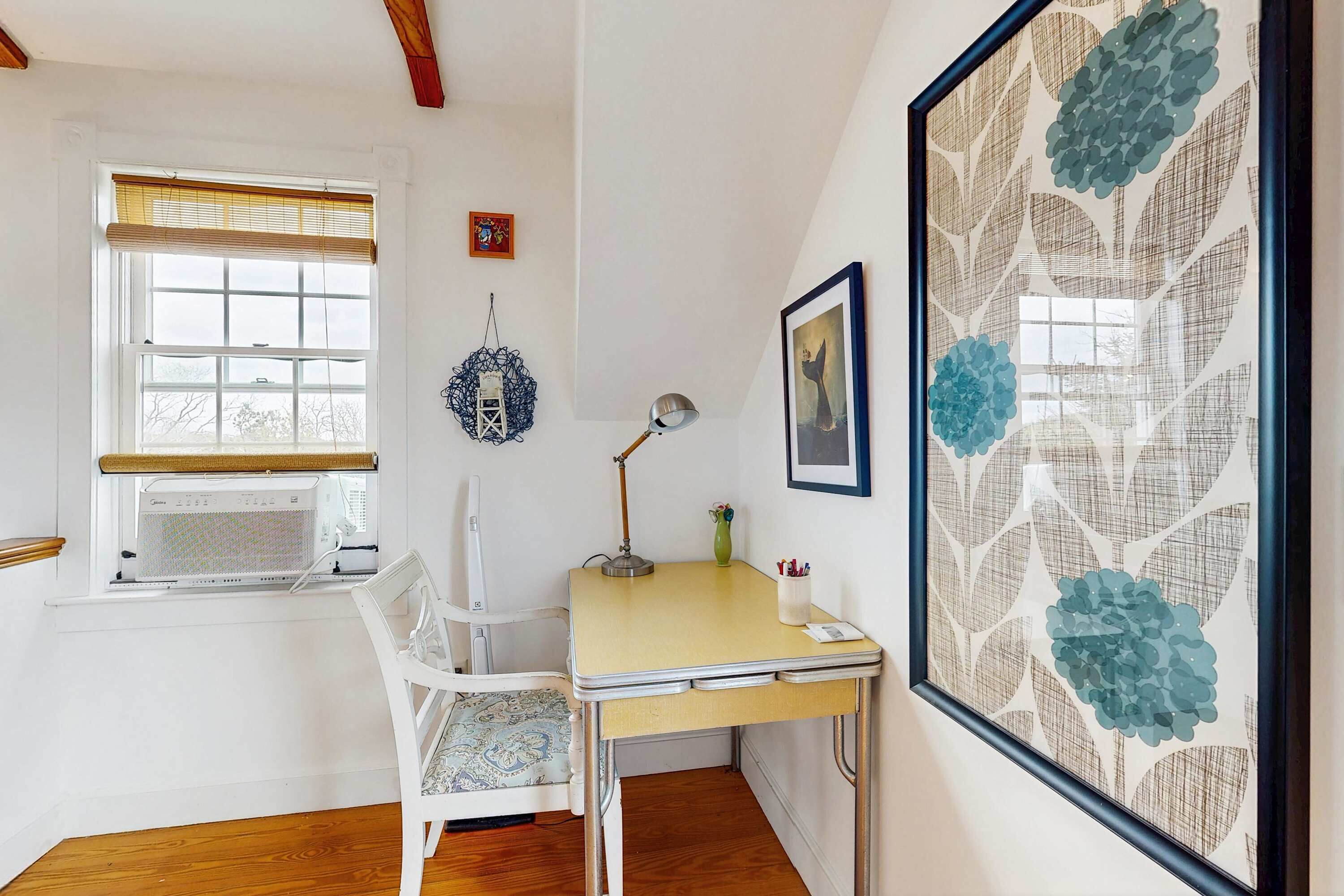 A room with a desk, chair, window, wall art, and a hanging decoration.