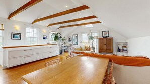 A spacious loft with high ceilings, exposed wooden beams, a dining area, a sofa, and a kitchen area.