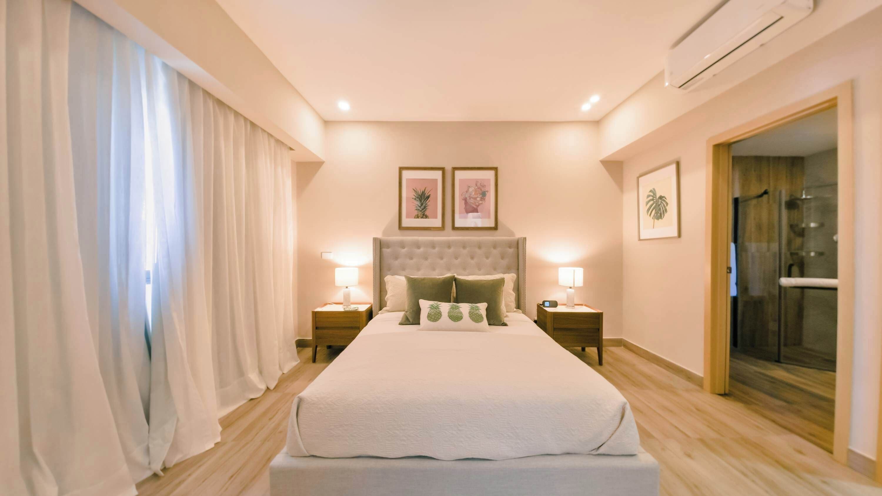 A bedroom with a large bed, two bedside tables, a headboard, and a shower area.