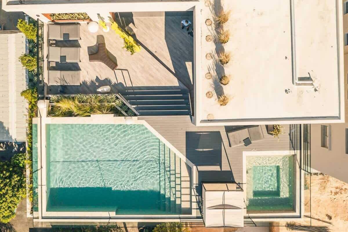 Eine Vogelperspektive eines modernen Resorts mit einem großen Schwimmbecken, einer Sonnenterrasse und einem Essbereich mit Außenbestuhlung.