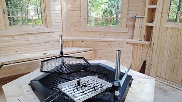 Une cabane en bois avec un espace barbecue, des bancs et de grandes fenêtres.