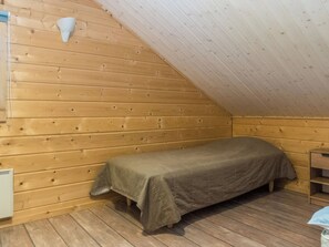 Ett litet rum med en enkel säng, träväggar och ett sluttande tak.