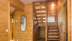 Ein Holzinnenraum mit einer Treppe zu einer oberen Ebene, einem Spiegel an der Wand und einer Tür zu einem weiteren Raum.