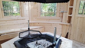 Eine Holzhütte mit Grillplatz, eingebauten Bänken und großen Fenstern.