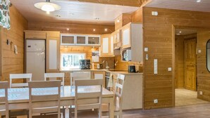Ein Holzinterieur mit einem Esstisch, Stühlen, einem Kühlschrank und einer Küchenzeile mit Schränken und einem Fenster.
