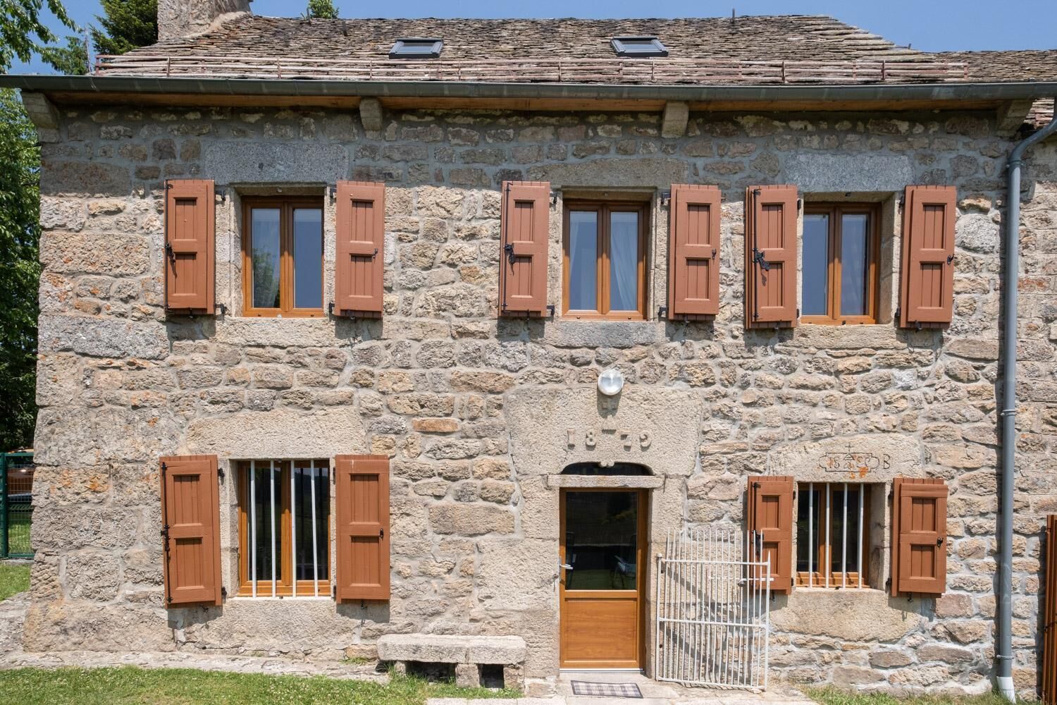 Un bâtiment en pierre avec des volets en bois, une porte et un petit banc.