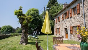 A stone building with wooden shutters, a grassy yard, and a yellow umbrella. - Les Fleurs de l'Aubrac 4/6 pers (SAINTE-COLOMBE-DE-PEYRE)
