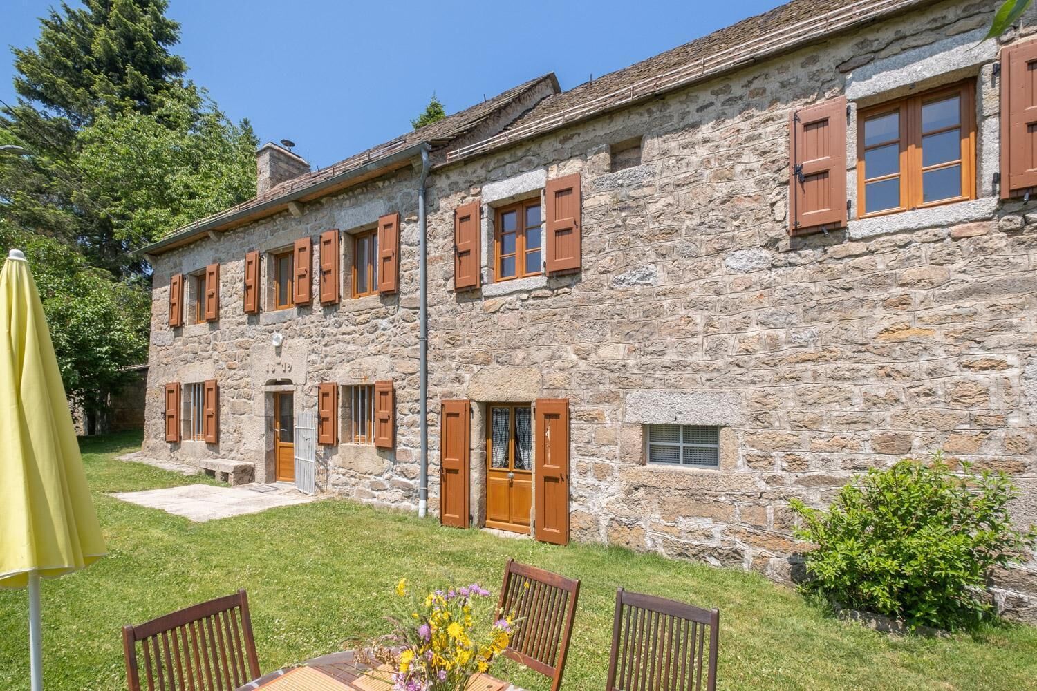 A stone building with multiple windows and doors, a grassy yard, and outdoor furniture.