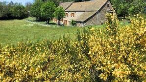 A stone house with a sloped roof, surrounded by a grassy field and trees. - Les Fleurs de l'Aubrac 4/6 pers (SAINTE-COLOMBE-DE-PEYRE)