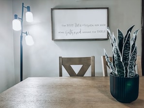 Ein Esstisch mit einem gerahmten Zitat, einer Topfpflanze und einer modernen Stehlampe.
