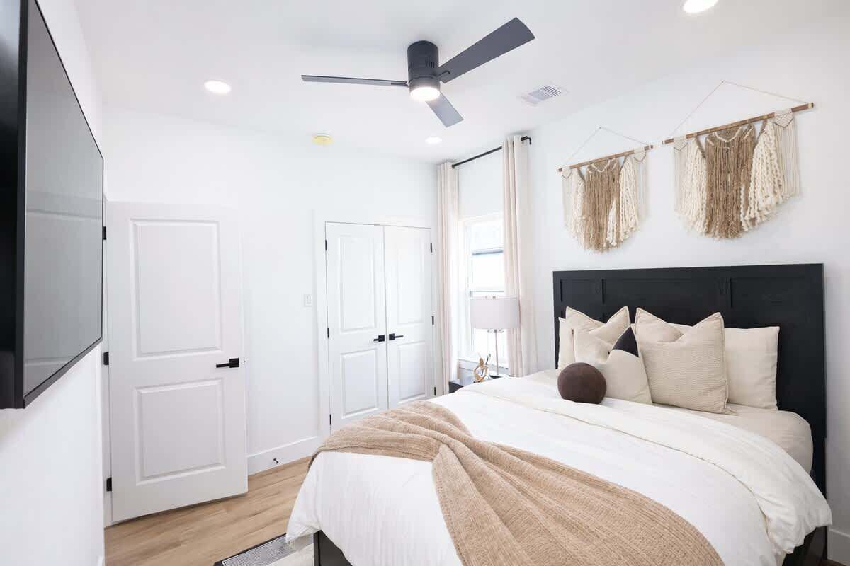 A bedroom with a bed, a ceiling fan, a TV mounted on the wall, and a door.