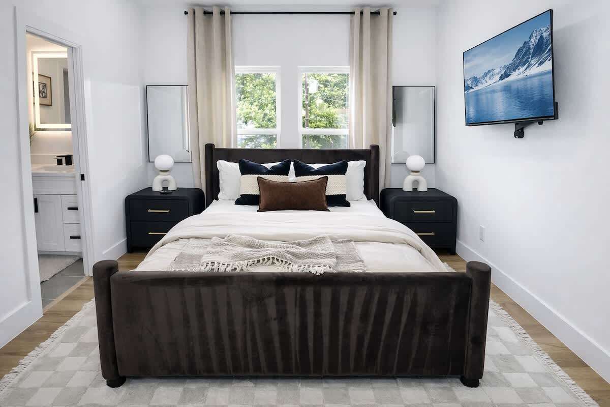 Een slaapkamer met een bed, nachtkastjes, een televisie en een raam met gordijnen.