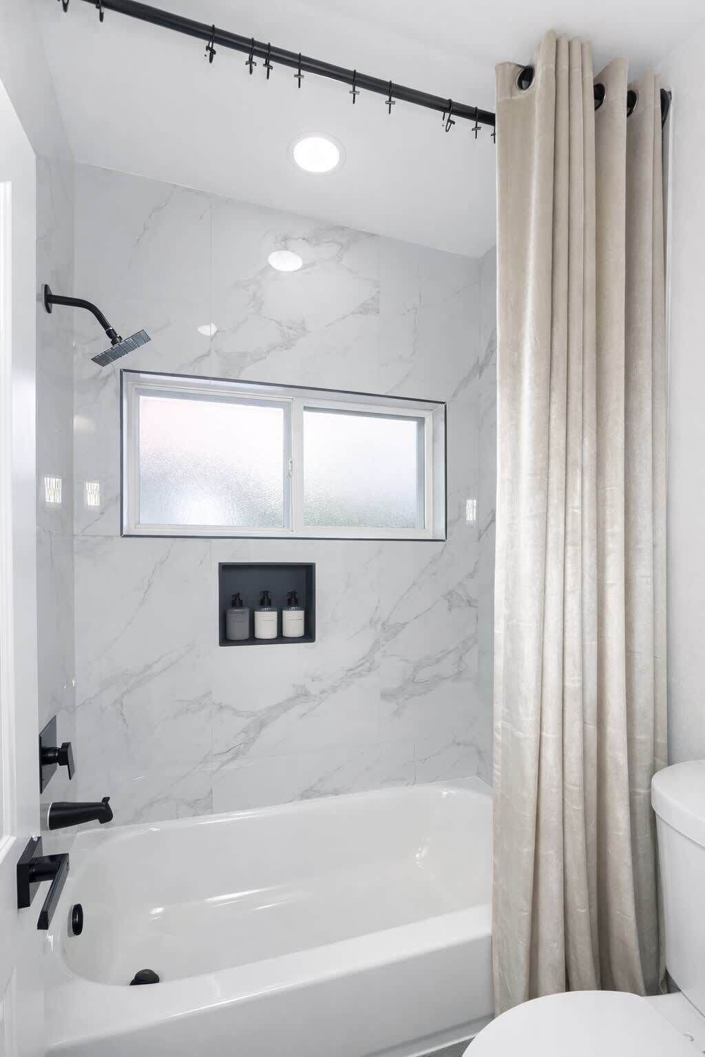 A bathroom with a bathtub, a showerhead, a window, and a toilet.