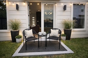 Un patio al aire libre con dos sillas, una mesa y plantas en macetas.