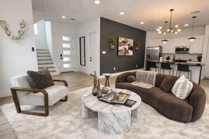 Una sala de estar moderna con un sofá, un sillón, una mesa de centro y una cocina al fondo.