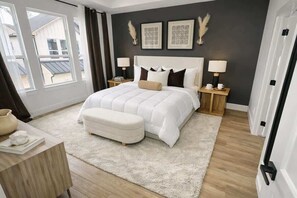 Un dormitorio con una cama grande, mesitas de noche, cortinas y vistas al exterior.
