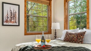 A bedroom with a bed, a bedside table with a bottle and glasses, a lamp, and a painting on the wall.