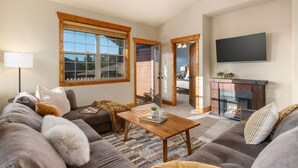 A living room with a sofa, a coffee table, a fireplace, and a television mounted on the wall.