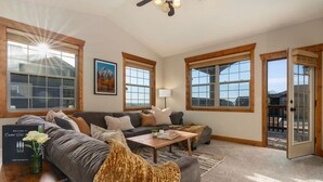 A spacious living room with a sofa, coffee table, and a fireplace. There are large windows and a door leading outside.