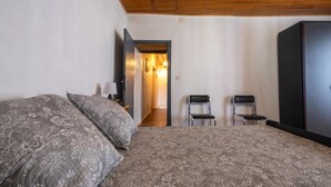 Quarto com cama, duas cadeiras, guarda-roupa e corredor que dá para outro espaço.