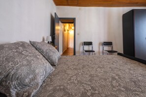 Ein Schlafzimmer mit einem Bett, zwei Stühlen, einem Kleiderschrank und einem Flur, der in einen anderen Raum führt.
